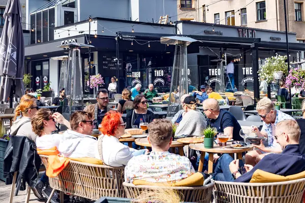 LATVIA, RIGA, JULY, 25, 2025: Riga Eski Kasabası, Letonya 'daki Livu Meydanı' nda bir restoranın açık verandasında öğle yemeği yiyen bir grup arkadaş