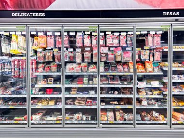 LATVIA, RIGA, AUGust, 12, 2025: Bir süpermarketteki çeşitli üreticilerin et lezzetleriyle dolu büyük cam buzdolabı. Riga. Letonya