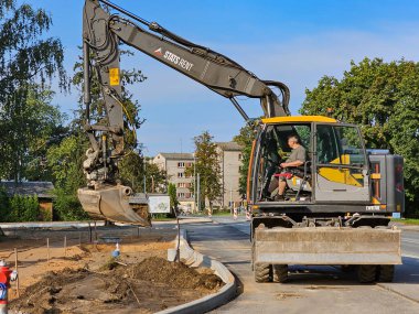LATVIA, RIGA, SEPTEMBER, 21, 2025: Bir işçi Riga, Letonya 'nın merkezinde onarılması gereken yollara kum saçan bir Volvo kazıcısını çalıştırıyor.