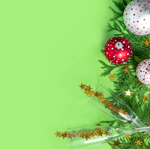 緑の紙の背景にシャンパンの木の枝や眼鏡を持つ多色のクリスマスボール 新年のクリエイティブグリーティングカード — ストック写真
