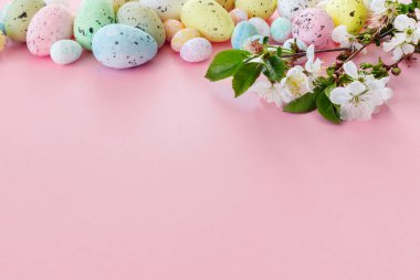 Renkli yumurtalar ve kağıt pembe arka planda kiraz dallarıyla güzel bir Paskalya kartı. Metnin için kopyalanmış çiçek tebrik kartı.