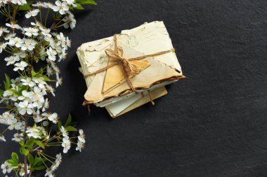 Stack of old torn vintage letters on yellowed paper against black granite table with cherry blossom branch