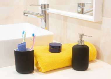 Toothbrush holder ,towel,cream and liquid soap dispenser near the sink at  bathroom .