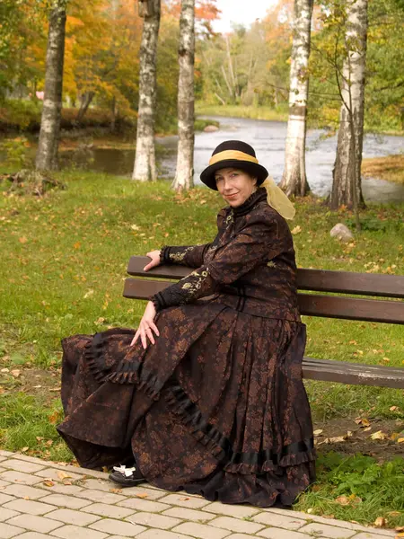 A woman in a Victorian dress sits on a park bench.