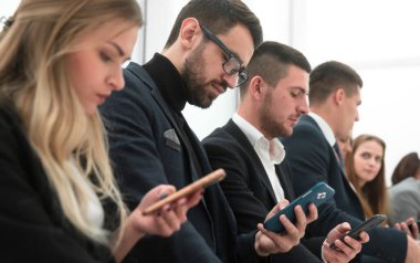 Kapat. Bir grup genç iş adamı akıllı telefon ekranlarına bakıyor..