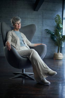 attractive middle aged smiling woman model sitting in chair looking at camera at office
