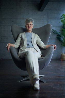 attractive middle aged smiling woman model sitting in chair looking at camera at office