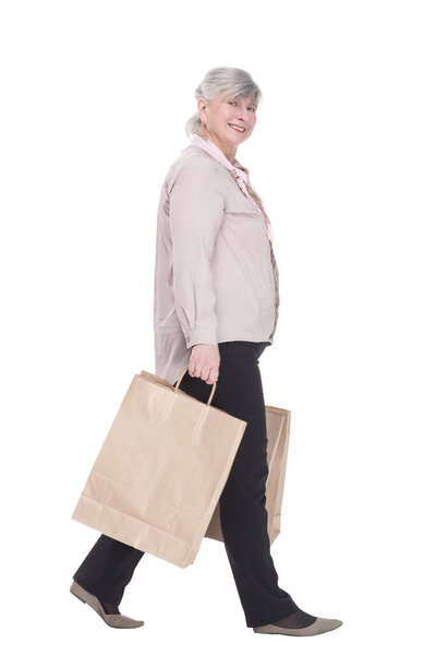 side view. smiling old lady with shopping bags striding forward . isolated on a white background.