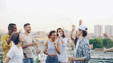 Ritim zevk kablosuz kulaklıklar giyen konsol karıştırma ile profesyonel Dj çalışırken mutlu arkadaşlar çatı partide dans ediyor. Arka planda güzel modern bir şehirdir.