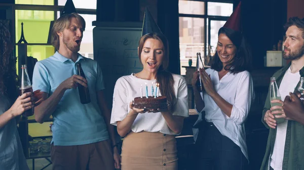 会社の従業員は誕生日を祝い 女性はケーキを持っていて ろうそくを笑って吹いていて 彼女の同僚は手を拍手しています — ストック写真