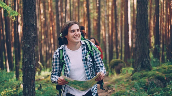 Joven Guapo Sostiene Mapa Camina Por Bosque Mientras Sus Amigos Imagen De Stock