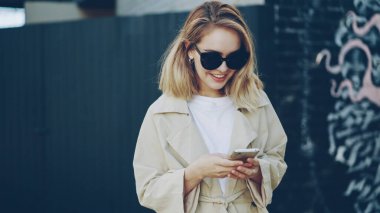 Mutlu genç kadın smartphone manifatura onun arkadaşı kullanarak ve grafiti resmi bulunan bir arka plan ile modern şehir açık havada duran gülümseyerek. İnsanlar, duygu ve teknoloji kavramı.