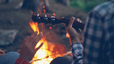 Yakın çekim erkek eller iskambil gitar ve eller ile kamp ateşi arka planda yanan dans hareket bir kadeh. Kamp, müzik ve maceracı insanlar kavramı.