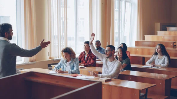 スマート男成功する学生は手を上げると教授に話を仲間の学生がそれらを聞いて 笑顔します 生徒と教師の関係概念 — ストック写真