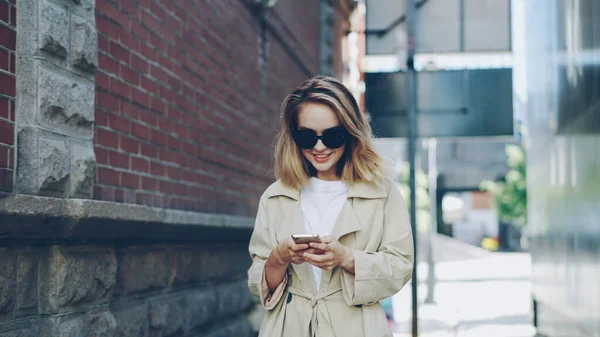 Hezká Blondýnka Používá Moderní Smartphone Dotýká Obrazovky Chůzi Městě Usmívá — Stock fotografie