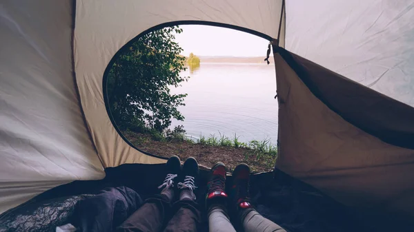 游客们躺在帐篷里移动脚做舞蹈动作有乐趣放松 美丽的湖泊或河流的风景是在外面 自然和野营概念 — 图库照片