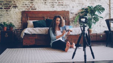 Uzun kıvırcık saçlı çekici genç kadın, internet blogu için kamera kullanarak video kaydediyor..