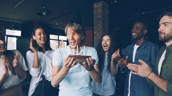 有表情的脸上有胡子的家伙在生日蛋糕上许愿 吹蜡烛 而他快乐的同事鼓掌祝贺他 — 图库照片