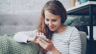 Mutlu genç kadın ekran dokunaklı ve sosyal medya hesabınızı kontrol veya metin mesajları okuma gülümseyerek smartphone tutuyor. Modern teknoloji ve millennials kavramı.
