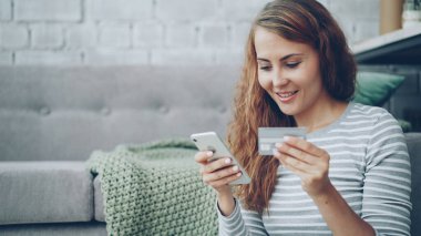 Heyecanlı genç bayan banka kartı tutan ve smartphone ekran dokunaklı o zaman mutlu bir şekilde gülümseyerek online ödeme yapıyor. Finans, internet alışveriş ve Alışverişkoliğin gençlik kavramı.