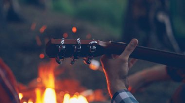 Yakın çekim sırasında romantik akşam kamp ile gitar erkek turistler el arka planda yanan ateş. Müzik aletleri, Doğa ve insan kavramı.