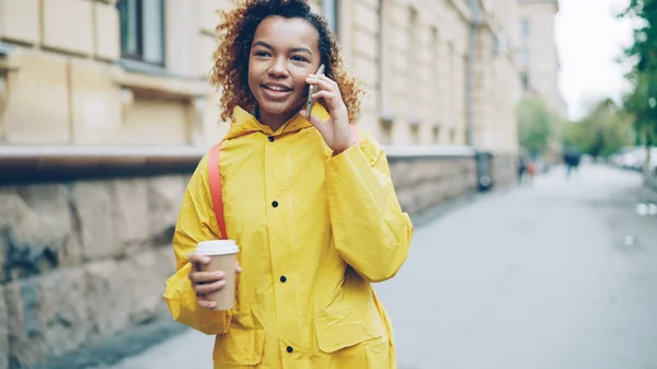 아프리카계 소녀가 스마트폰으로 이야기하면서 아름다운 도시의 거리를 커피를 있습니다 — 스톡 사진