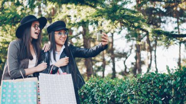 Heyecanlı kız mermiyi tutuyor ve alışveriş torbaları alımları ile gösterilen smartphone kullanarak online video arama yapıyoruz. İletişim, modern teknoloji ve eğlence kavramı.