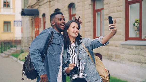 Ευτυχισμένοι Τουρίστες Φίλοι Σακίδια Παίρνουν Selfie Χρησιμοποιώντας Smartphone Δείχνει Χειρονομίες — Φωτογραφία Αρχείου