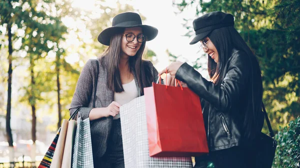 兴奋的女孩看着她的朋友购物袋 问价格和收集问题 并表示兴奋的购物站在一起在城市的街道上 — 图库照片