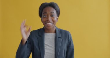 Afro-Amerikalı mutlu iş kadınının portresi el hareketi yapıyor ve sarı arka planda gülümsüyor. Pozitif duygu ve iş insanları kavramı.
