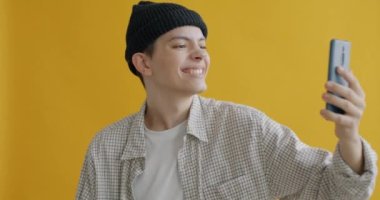 Akıllı telefon kamerasına poz veren mutlu bir çocuğun portresi selfie çekiyor ve sarı arka planda baş parmak hareketi gösteriyor. Aygıt ve fotoğraf konsepti.