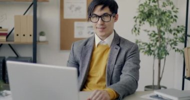 Ofisteki kameraya gülümseyen Asyalı neşeli girişimcinin yavaş çekim portresi. İnsan ve iş kavramı.