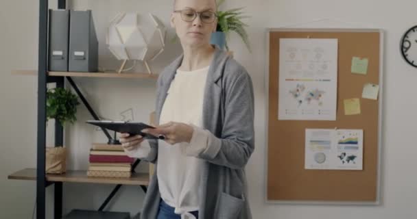職場を歩いて書類を読み ノートパソコンを持ってデスクに座っている女性のオフィスワーカー 事業活動と書類のコンセプト — ストック動画