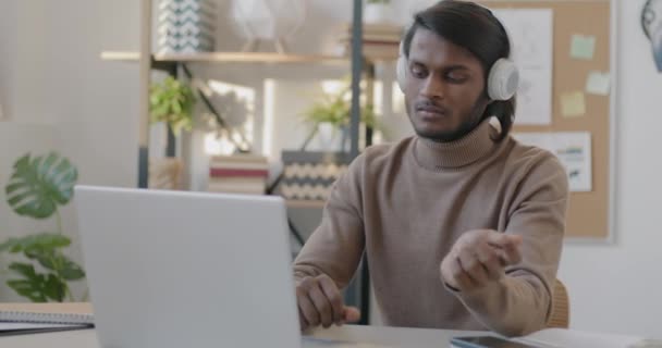 ノートパソコンを使ってヘッドフォンで音楽を聴き 職場で踊る陽気なインド人の肖像 仕事と娯楽の概念 — ストック動画