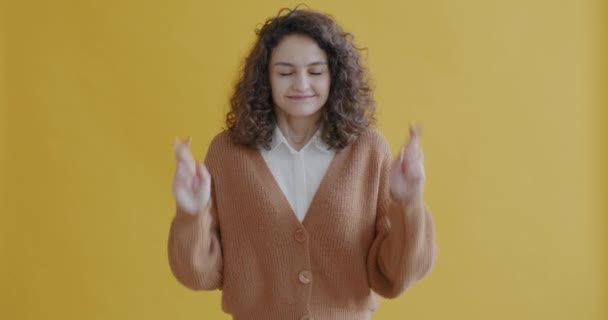 年轻学生的画像 在黄色的背景上 用手指许愿 闭目微笑 人与表达的概念 — 图库视频影像