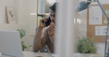Dizüstü bilgisayarla çalışan Hintli müdürün portresi ve ofiste cep telefonuyla konuşması. İş iletişimi ve gençlerin kavramı.