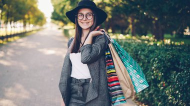 Kağıt tutan genç ve güzel kadın portresi açık havada şehirde ayakta ve güneşli sonbahar gününde kameraya bakarak çanta. Alışveriş, modern Gençlik ve sokak kavramı.