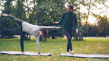 Dost yoga eğitmeni Half Moon poz Ardha Chandrasana'dan korumak için yardım kız öğrencinin yanına, konuşan duruyor ve onu tutan el ve bacak profesyonel.