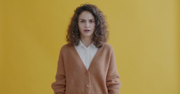 カメラを見ている緊張した若い女性のスローモーションポートレート顔に触れ 黄色の色の背景にジェスチャー 人と表現の概念 — ストック動画