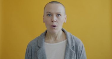 Şok olmuş, ağzı açık, sarı arka plandaki büyük gözlerle kameraya bakan kadının yavaş çekimde portresi. İfadeler ve insanlar konsepti.