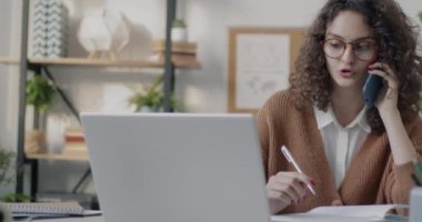 Genç ofis çalışanı cep telefonuyla konuşuyor ve ofiste tek başına çalışıyor. Kurumsal iletişim ve teknoloji kavramı.