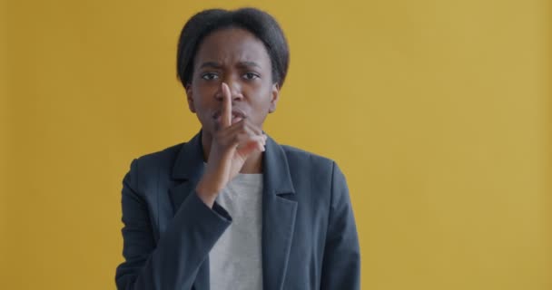 严肃的非洲裔美国女商人的画像 她做着沉默的手势 看着镜头 要求在黄色背景上保持安静 人与表达的概念 — 图库视频影像