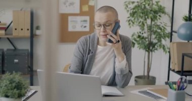 Başarılı bir genç kadın cep telefonuyla konuşuyor ve bilgisayarını ofiste yalnız çalışıyor. Modern iletişim ve işyeri kavramı.