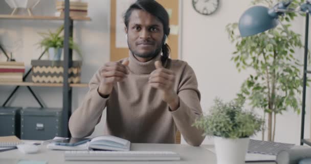 オフィスでの音声通話やイヤホンを使ったジェスチャーでオンラインビデオ通話を行うインド人男性の肖像 ビジネスコミュニケーションとテクノロジーの概念 — ストック動画