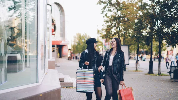 时尚的年轻女性朋友们走在街上 拿着纸袋购物 看着商店橱窗从新的收藏品中挑选时髦的服装 — 图库照片