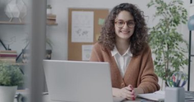 İş yerinde oturmuş kameraya gülümseyen neşeli iş kadınının yavaş çekim portresi. Modern insanlar ve girişimci konsepti.