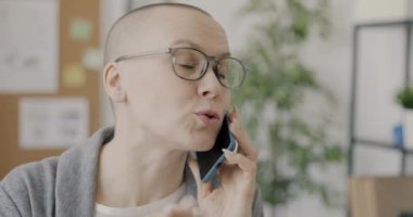 Kendine güvenen genç bir iş kadını cep telefonuyla konuşuyor ofiste yalnız çalışıyor ve iş konuşuyor. İşyeri ve kablosuz teknoloji kavramı.