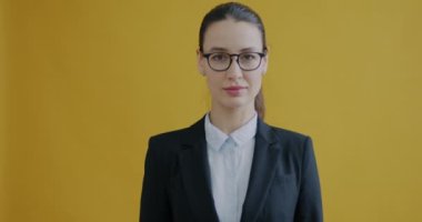 Takım elbiseli kadının portresi sessizlik istiyor sarı arka planda parmakları olan dudaklara dokunuyor. İş insanları ve ifade kavramı.