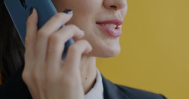 Sarı arka planda cep telefonuyla konuşan resmi giyinmiş genç bir kadının yakın çekimi. Modern teknoloji ve iş iletişimi kavramı.
