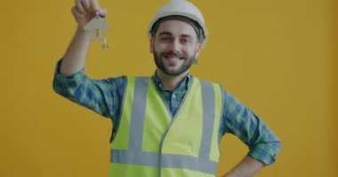 Şen şakrak inşaat müdürünün ev anahtarını tutması ve sarı arka planda gülümsemesi. Emlak ve konaklama konsepti oluşturuluyor.